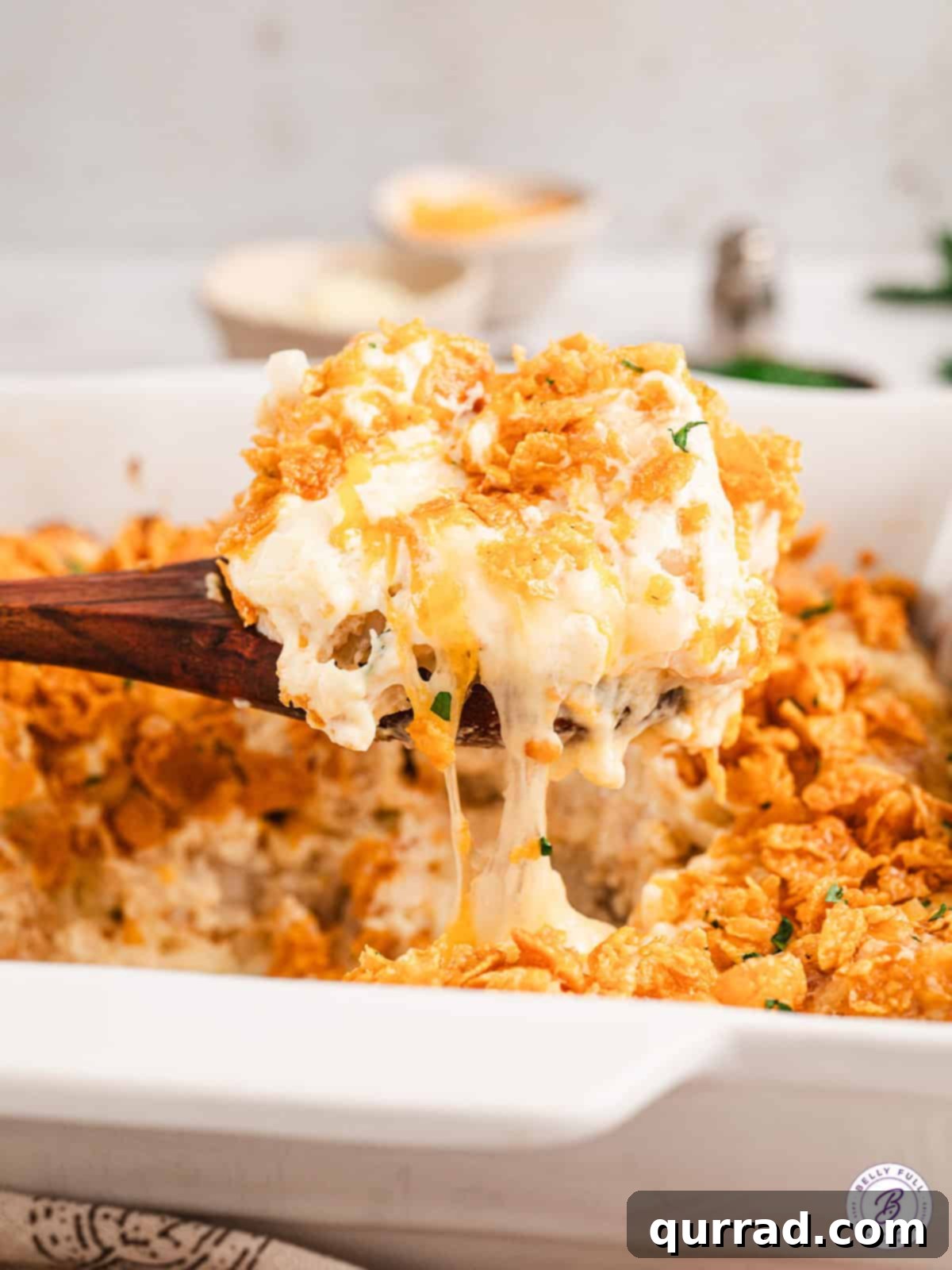 wooden spoon serving a scoop of cheesy funeral potatoes from a casserole dish
