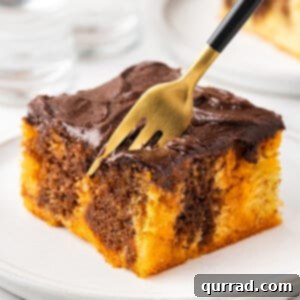 Witches' Brew Poke Cake 5 A slice of Halloween Poke Cake on a white plate with a fork, showcasing distinct orange and chocolate layers.
