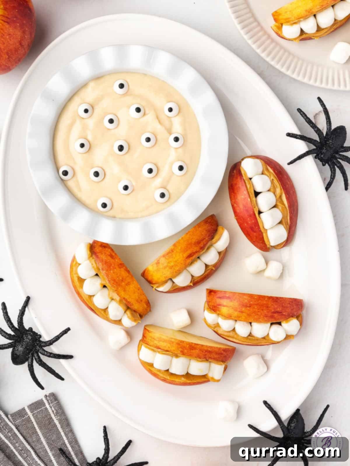 Apple Creature Chompers with Fruity Dip 3 Overhead shot of Apple Monster Mouths arranged around a bowl of orange Monster Fruit Dip adorned with edible candy eyes for a festive Halloween spread.