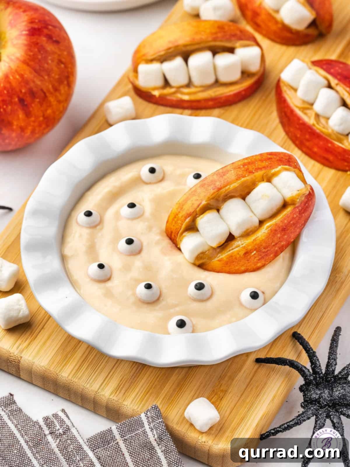 Apple Creature Chompers with Fruity Dip 4 A close-up of an apple monster mouth being dipped into the vibrant orange Monster Fruit Dip with floating edible eyes.