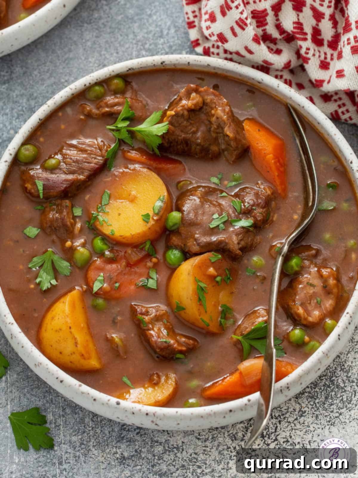 Close-up of beef stew served in a rustic bowl with a spoon, showing chunky carrots, potatoes, and tender beef in a thick, rich broth.