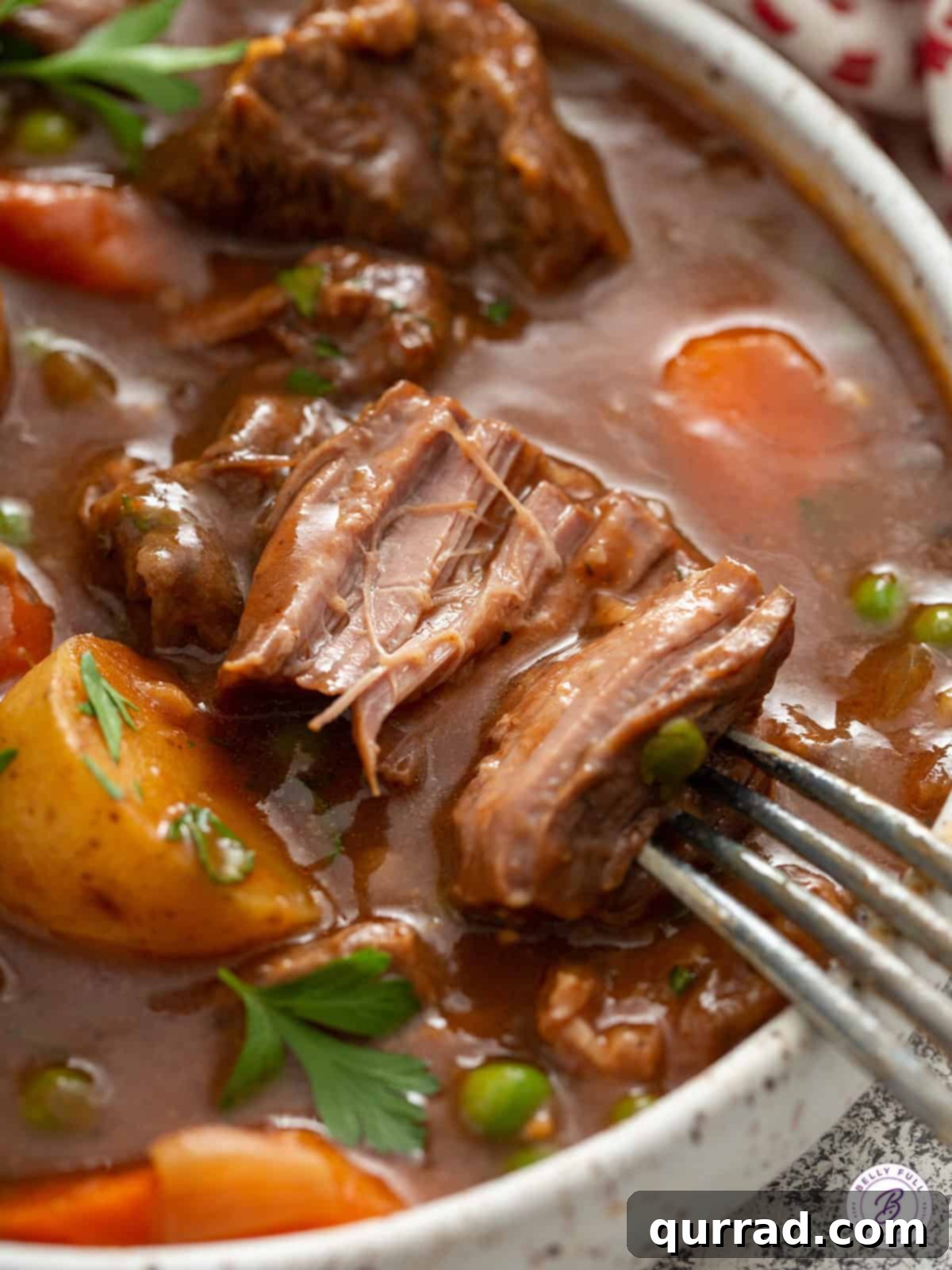A fork gently shredding a piece of perfectly tender stew meat, demonstrating its melt-in-your-mouth texture achieved through slow cooking.