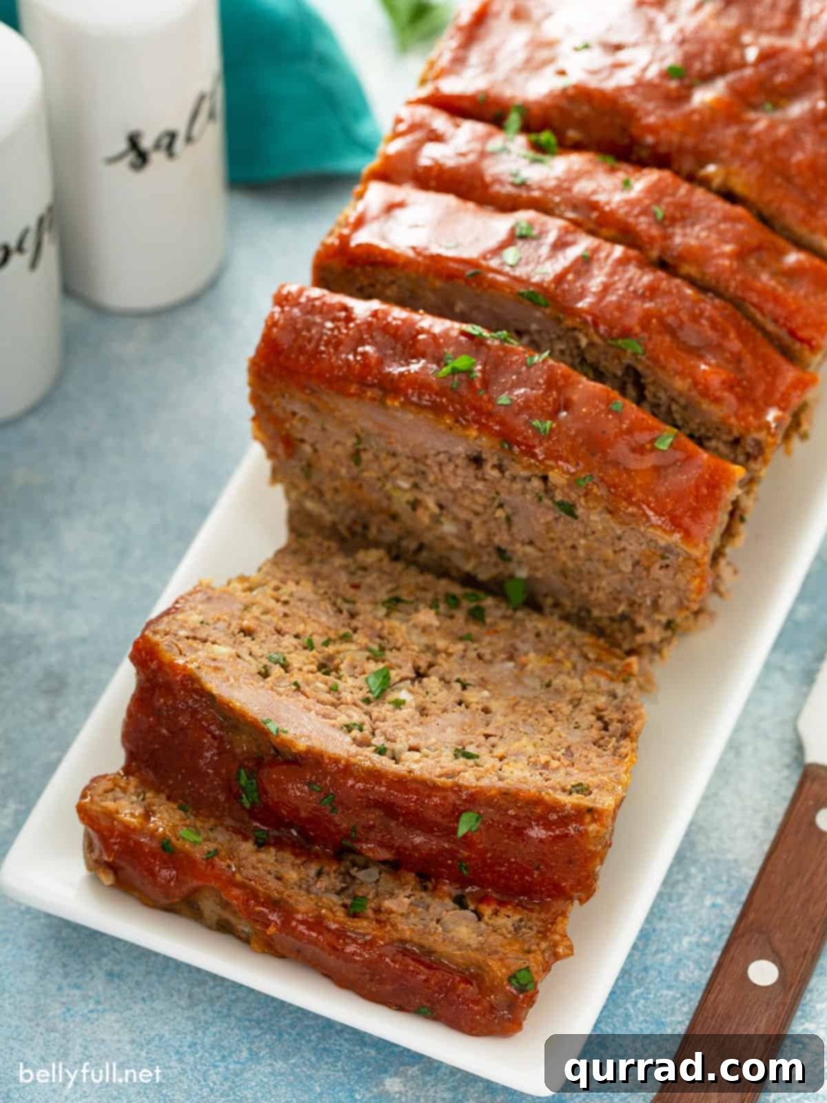 Sliced glazed meatloaf on a white serving plate, showing its tender interior and rich crust.