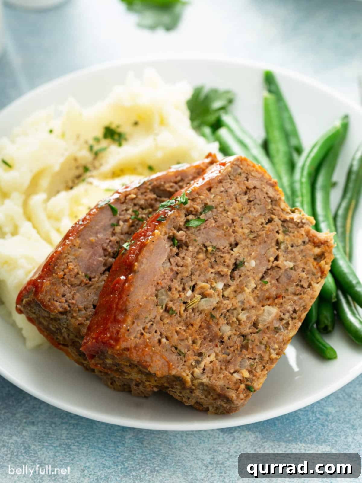 Two slices of classic meatloaf served on a plate with creamy mashed potatoes and vibrant green beans.
