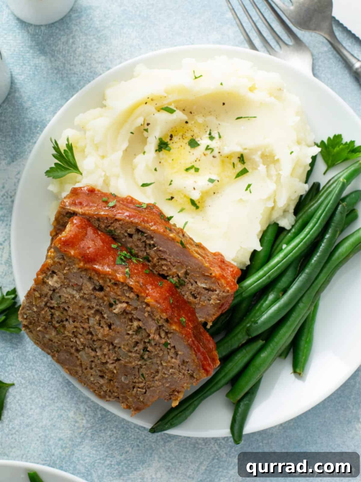 Two slices of classic meatloaf served on a plate with creamy mashed potatoes and vibrant green beans.