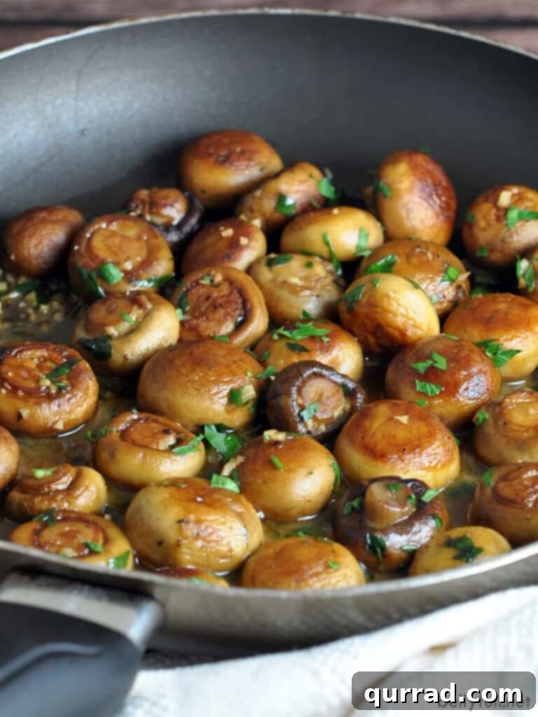 Sautéed Mushrooms with Garlic and Herbs 2 A close-up view of whole sautéed button and cremini mushrooms glistening in a skillet with a rich pan sauce.