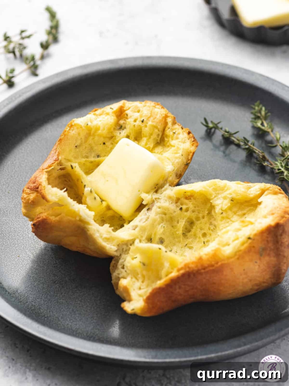 Fluffy Cheesy Popovers 5 popover split in half with pat of butter and thyme on plate