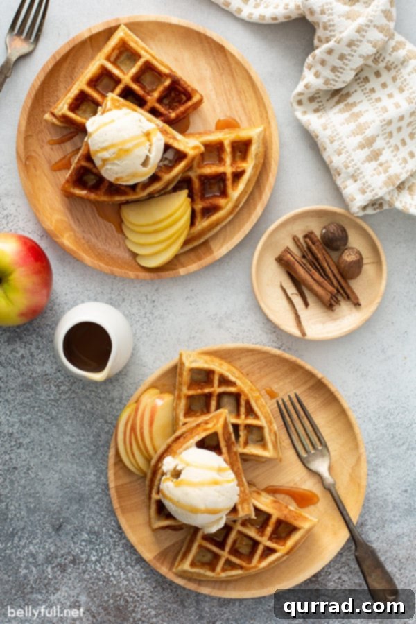 Apple Pie Waffles Ready to Serve Overhead shot of two plates of apple pie waffles, each topped with a scoop of vanilla ice cream and drizzled with caramel sauce, arranged on a rustic wooden table.