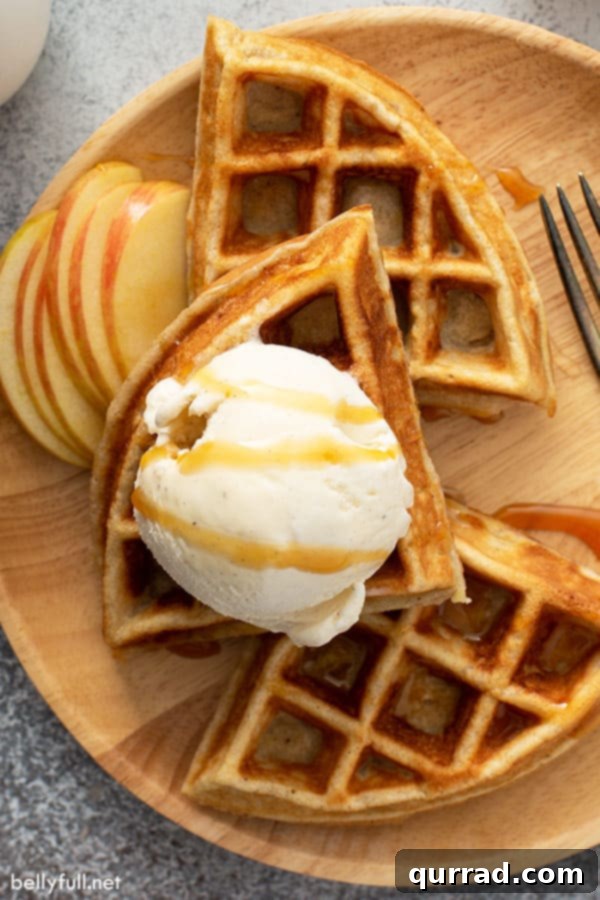 Spiced Apple Waffles 3 An inviting close-up overhead shot of an apple pie waffle stack, generously topped with melting vanilla ice cream and a drizzle of caramel, ready to be served.