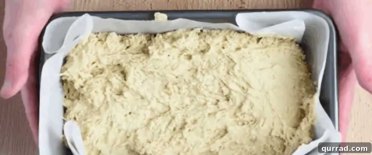 Beer bread batter being spooned into a prepared loaf pan.