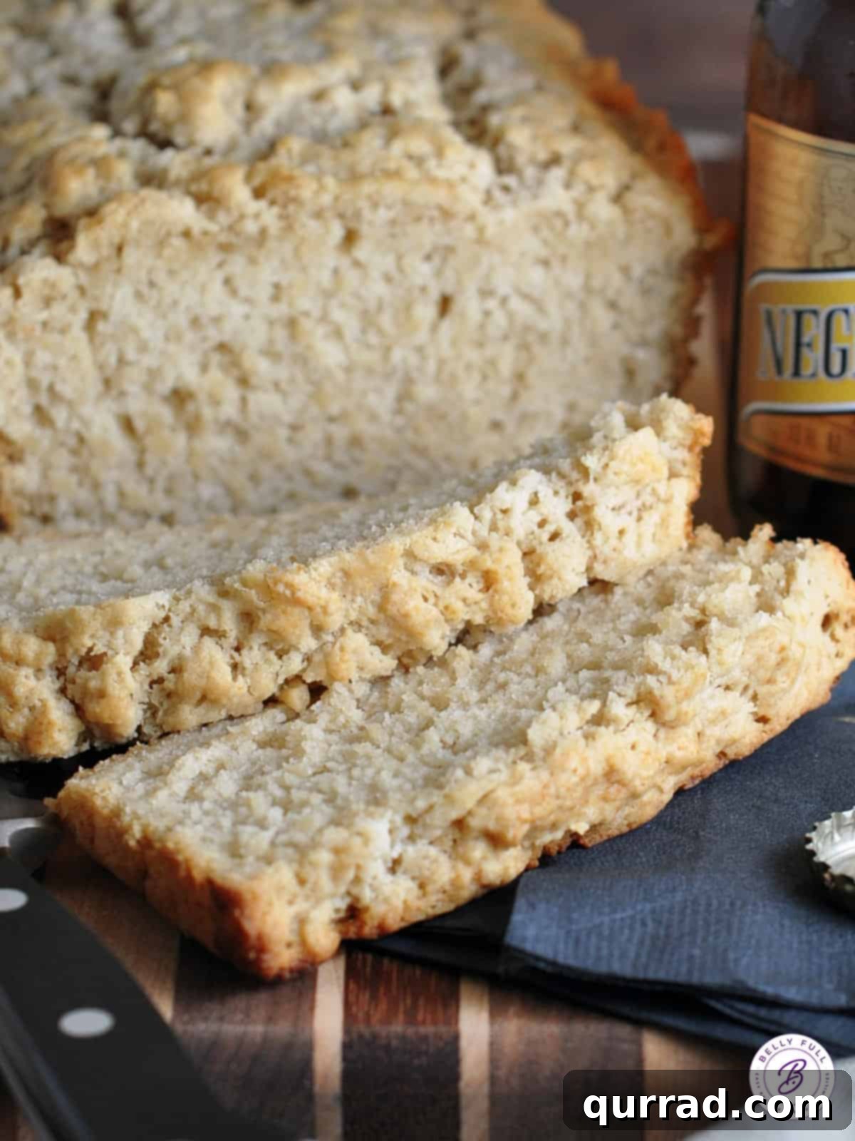 Two slices of freshly baked beer bread resting next to a bottle of beer, emphasizing its texture.