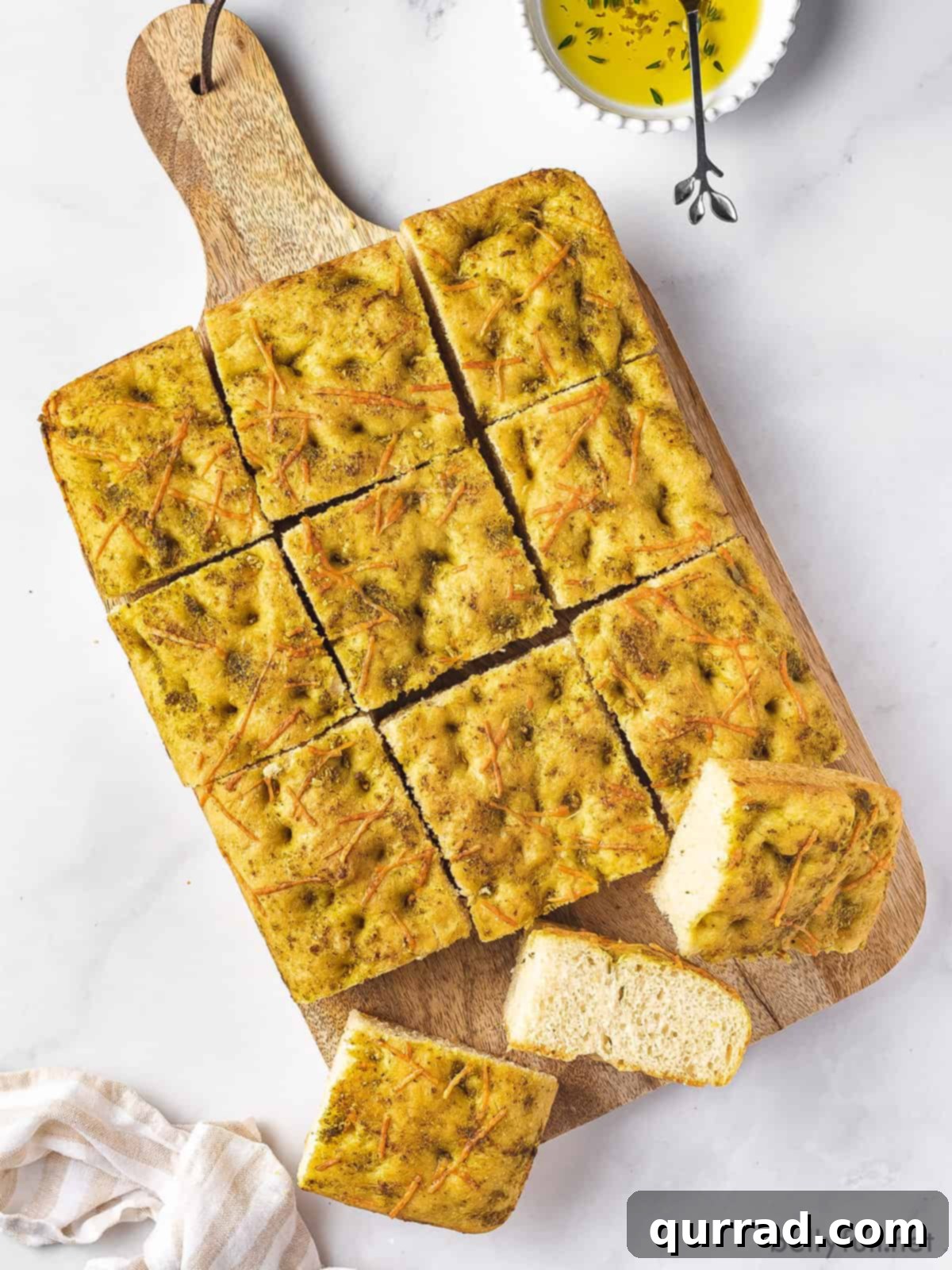 Savory Rosemary Focaccia 4 Focaccia bread, generously topped with pesto and Parmesan, cooling on a wooden cutting board after being sliced into individual squares.