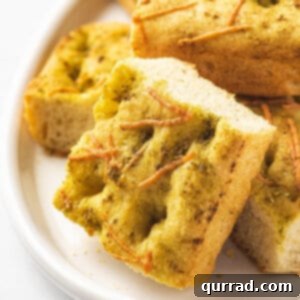 Close up of a piece of focaccia bread on a white plate, showing the pesto and Parmesan topping