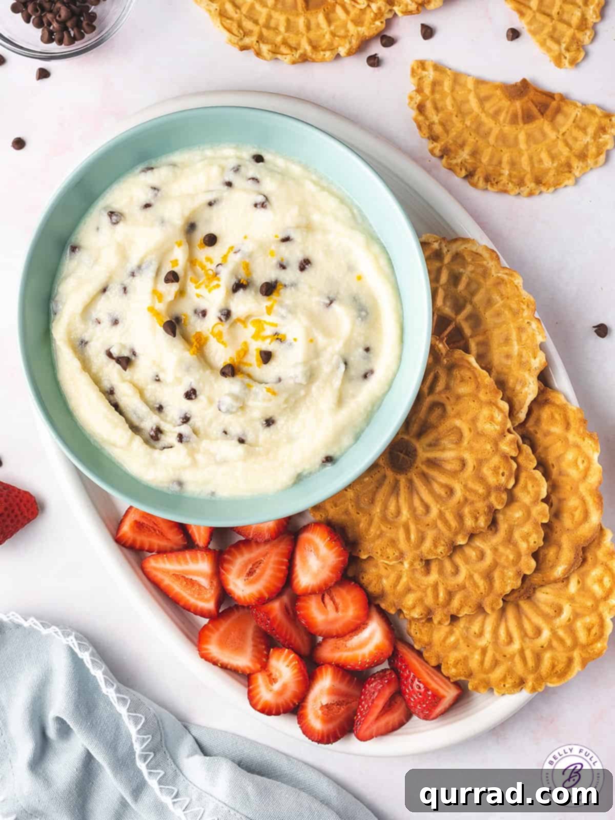 Overhead view of a bowl of cannoli dip presented on a plate with fresh strawberries and crispy waffle cookies for dipping.