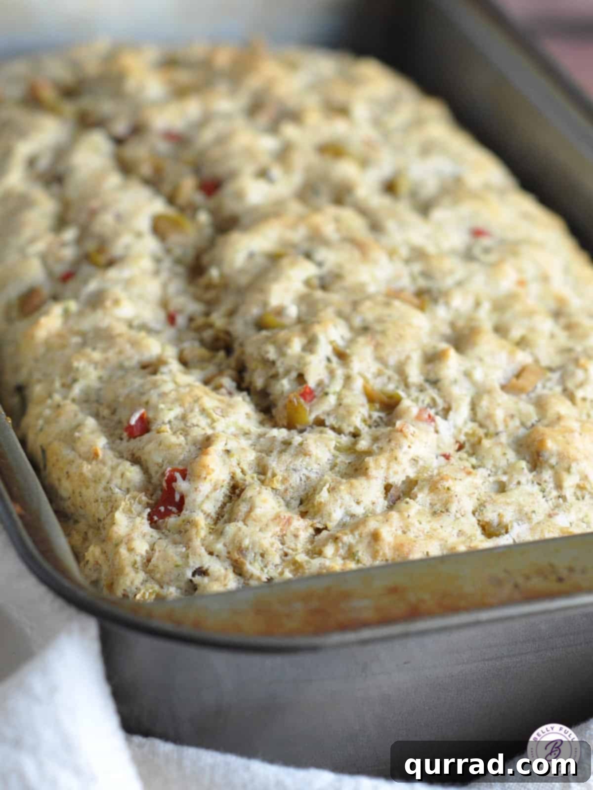Mediterranean Olive Loaf 3 A freshly baked loaf of olive quick bread cooling in a loaf pan, displaying its golden-brown crust.
