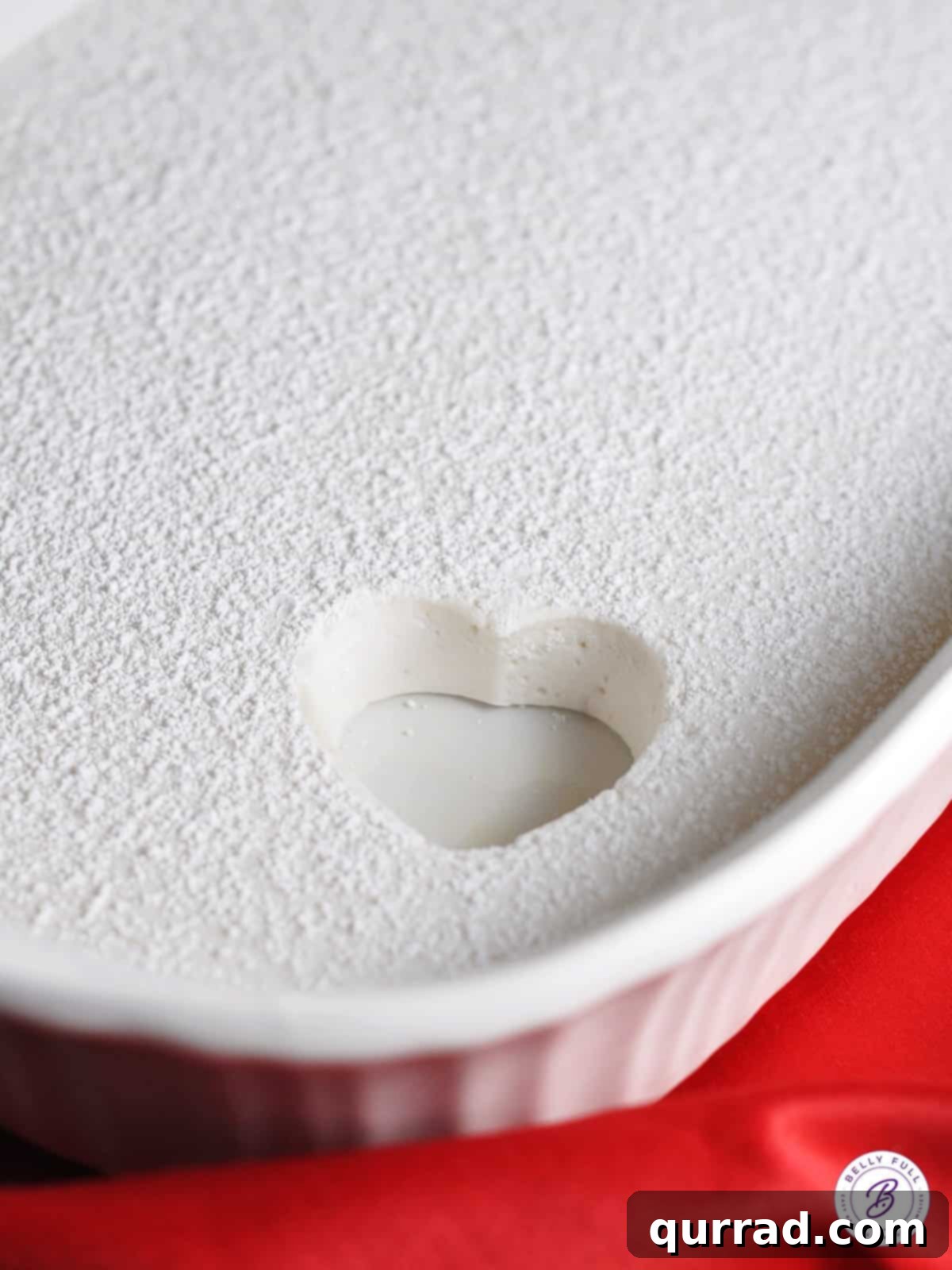 Close-up of a pan of marshmallow slab with a heart-shaped cookie cutter pressing down, ready to cut.