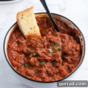 Bolognese sauce in bowl with slice of garlic bread