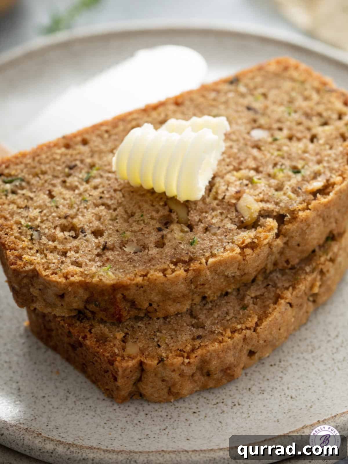 Two perfectly baked slices of zucchini loaf cake, ready to be enjoyed with a small pat of butter on top.