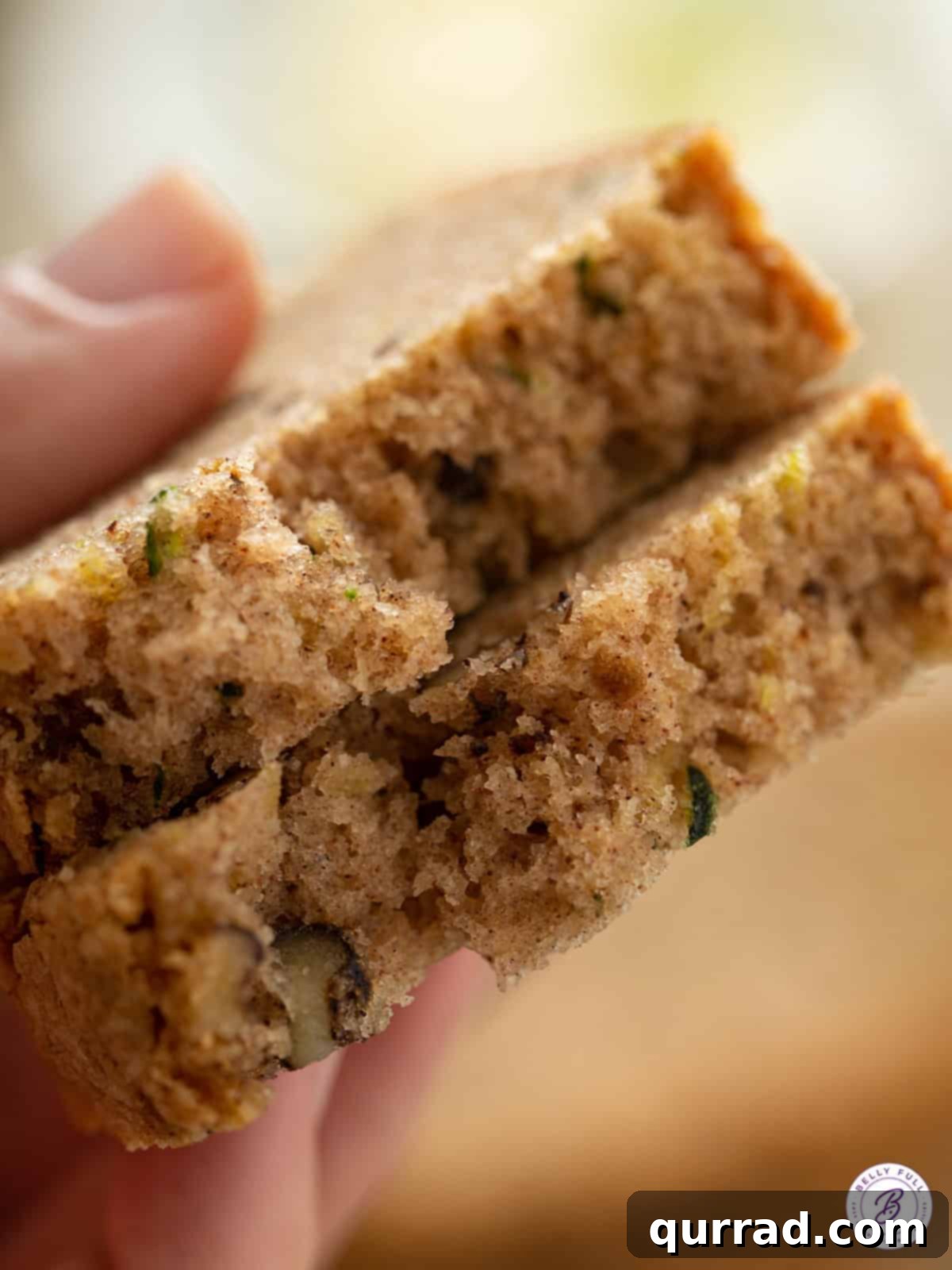 A close-up view of a thick slice of fluffy Zucchini Bread, cut in half to show its moist, tender crumb and speckles of walnuts.