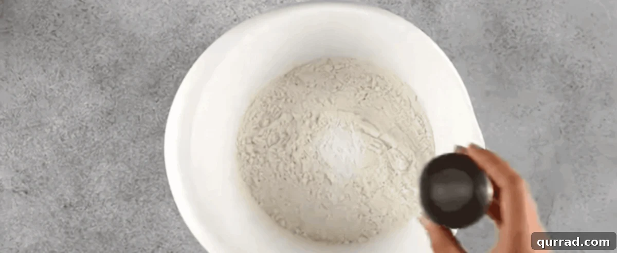 A close-up image showing dry ingredients like flour, baking soda, and cinnamon being whisked together in a large bowl.