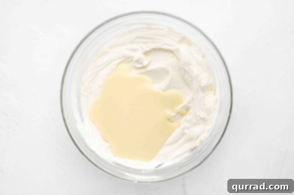 whipped cream being folded into melted white chocolate in a glass bowl