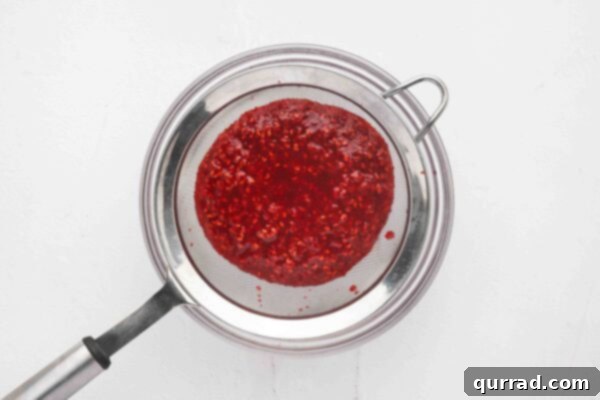 raspberry sauce being strained through a fine-mesh sieve into a glass bowl