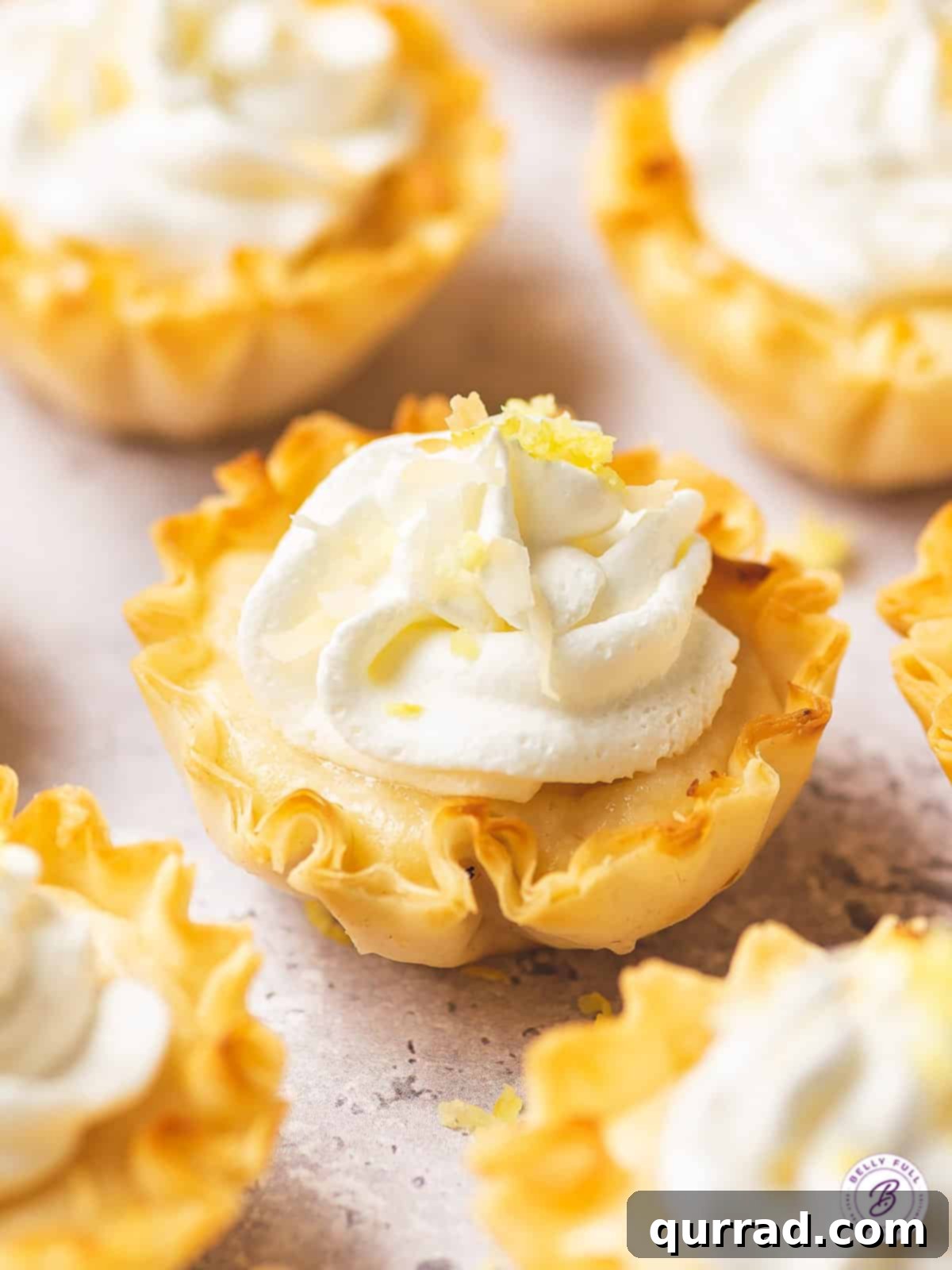 Effortless Tangy Lemon Tartlets 2 close up mini lemon tart with whipped cream and lemon zest