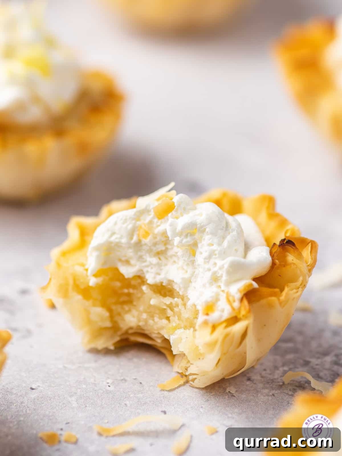 Effortless Tangy Lemon Tartlets 5 mini lemon tart with whipped cream and bite taken