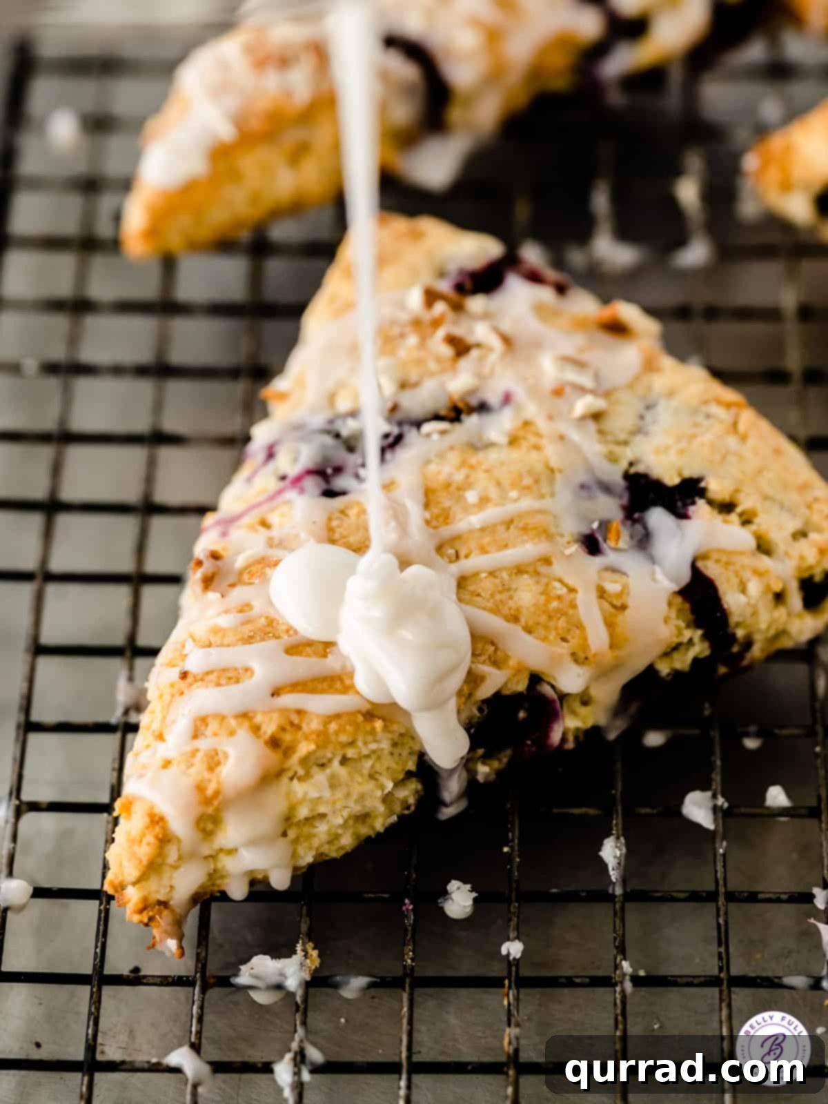 Tender Almond Blueberry Scones 3 Close-up shot of creamy white icing being drizzled generously on top of a freshly baked scone, showcasing the silky texture of the glaze.