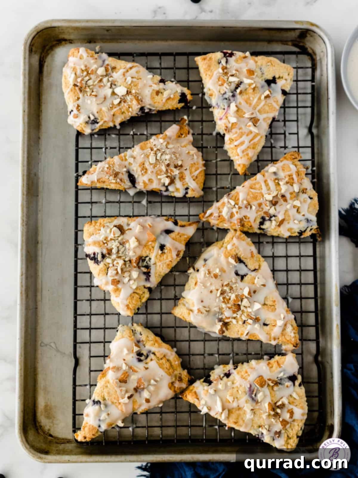 Tender Almond Blueberry Scones 4 Eight perfectly triangular glazed almond blueberry scones arranged neatly on a wire baking rack, cooling down after being freshly baked.