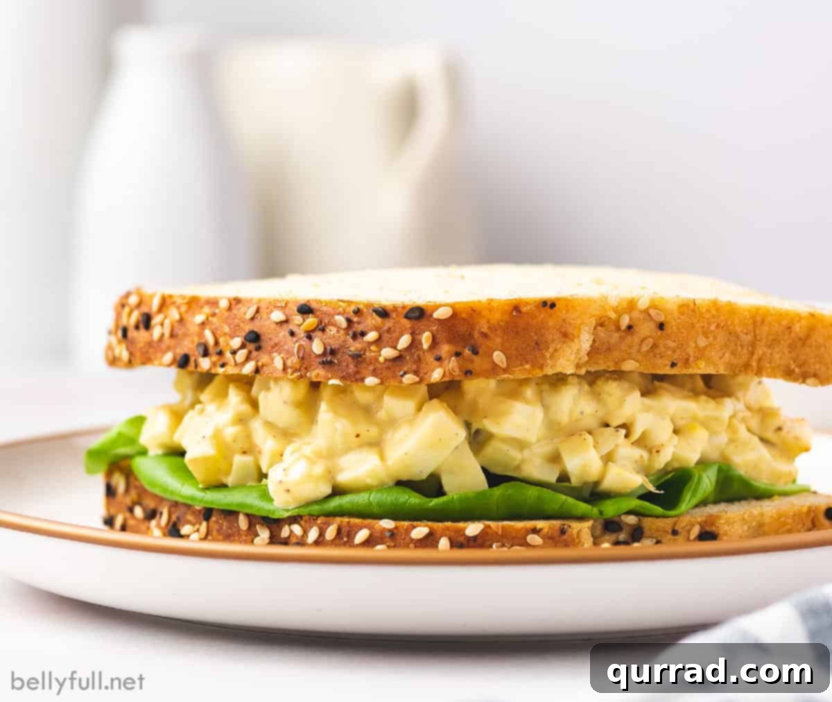 Creamy Egg Salad 7 A perfectly prepared egg salad sandwich, cut diagonally, served on a white plate with fresh lettuce and a side of potato chips, ready to be enjoyed.
