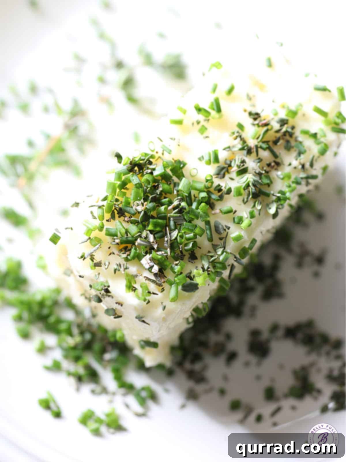 block of butter with fresh chopped herbs on top, ready to be mixed
