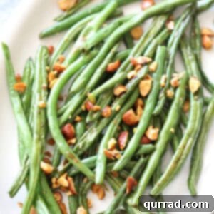 Overhead view of perfectly roasted green beans with chopped Sriracha almonds on a serving platter, ready to be enjoyed.