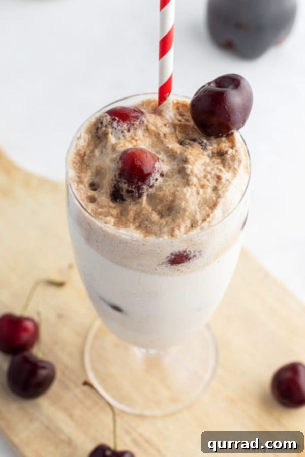 Cherry Cloud Float 2 Close-up of a vibrant cherry ice cream float in a tall glass, garnished with fresh cherries and a red and white straw.