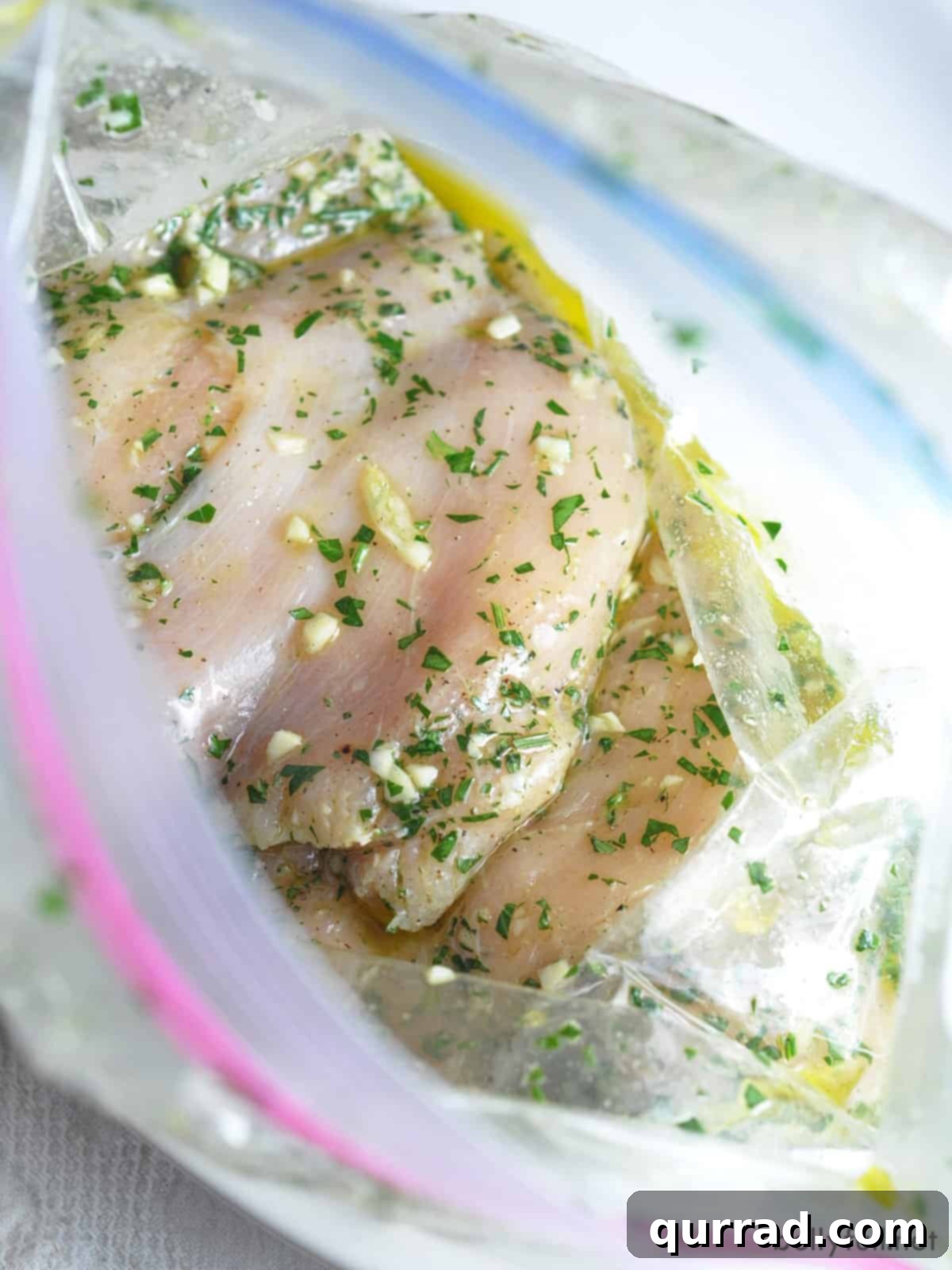 Juicy Grilled Chicken Breasts 4 Raw chicken breasts marinating in a plastic bag with herbs and lemon.