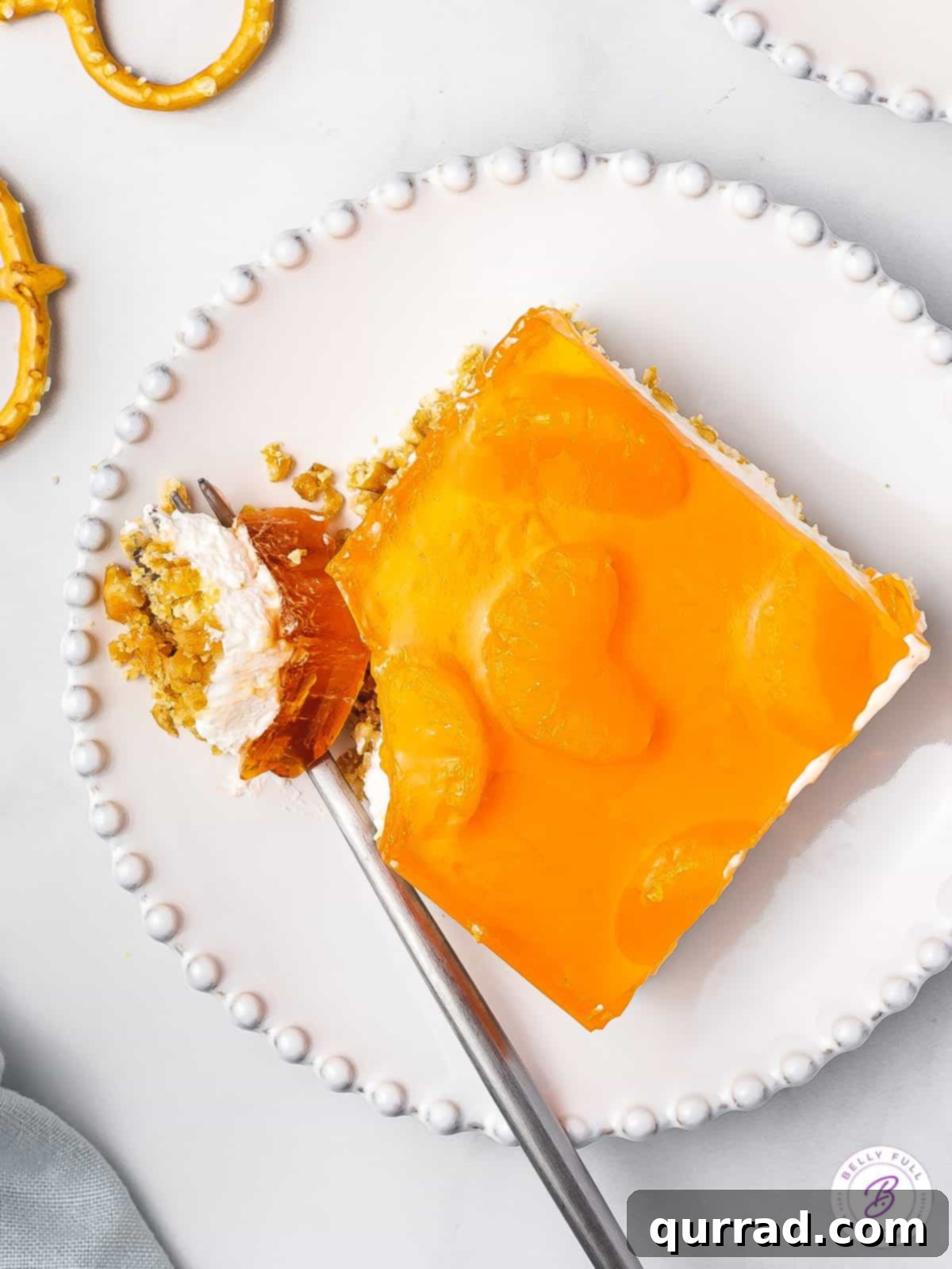 overhead piece of orange pretzel jello on fork on white plate, showcasing the layers