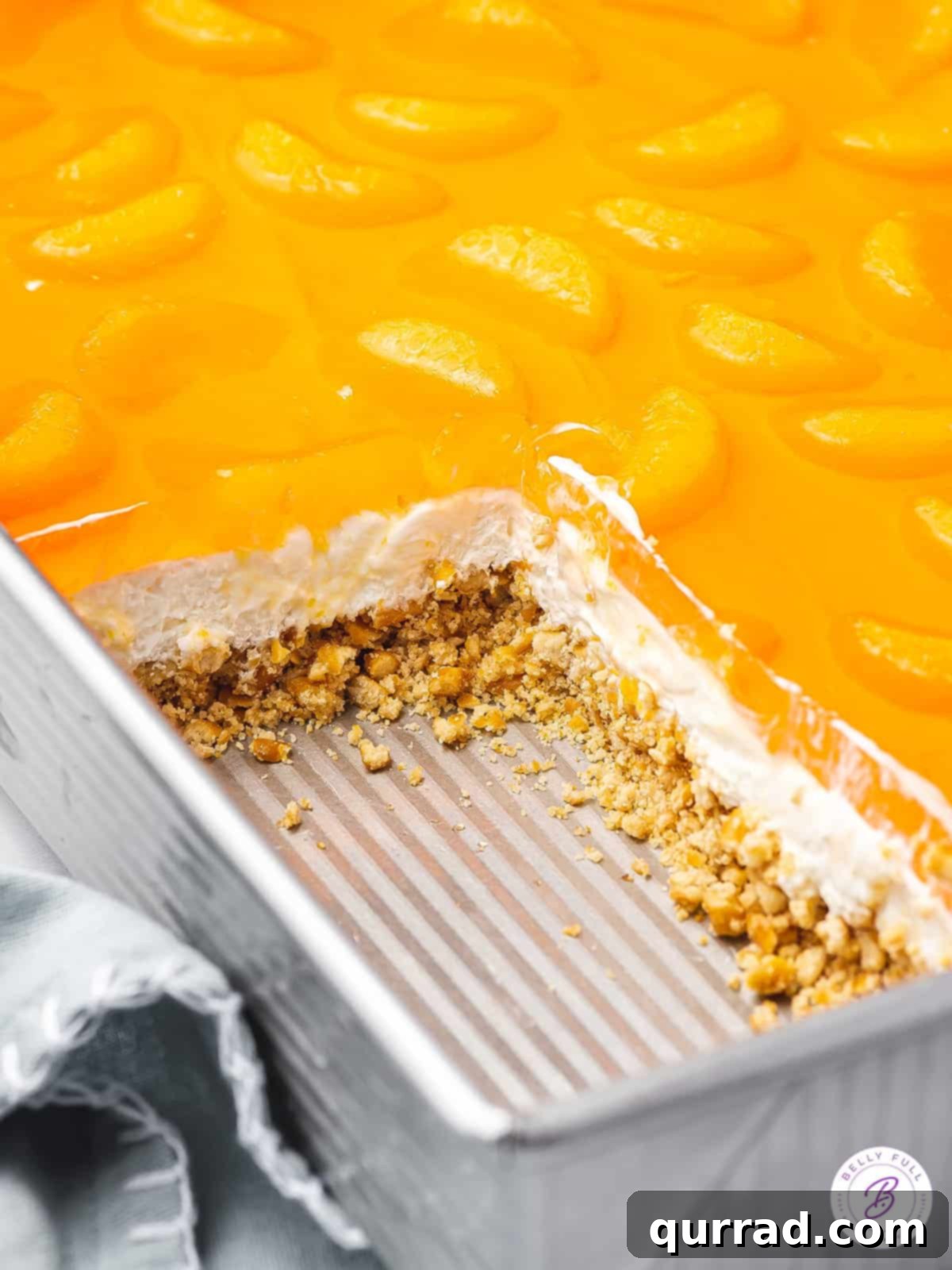 layers of orange pretzel salad dessert exposed in casserole pan, showing the distinct pretzel, cream cheese, and jello layers