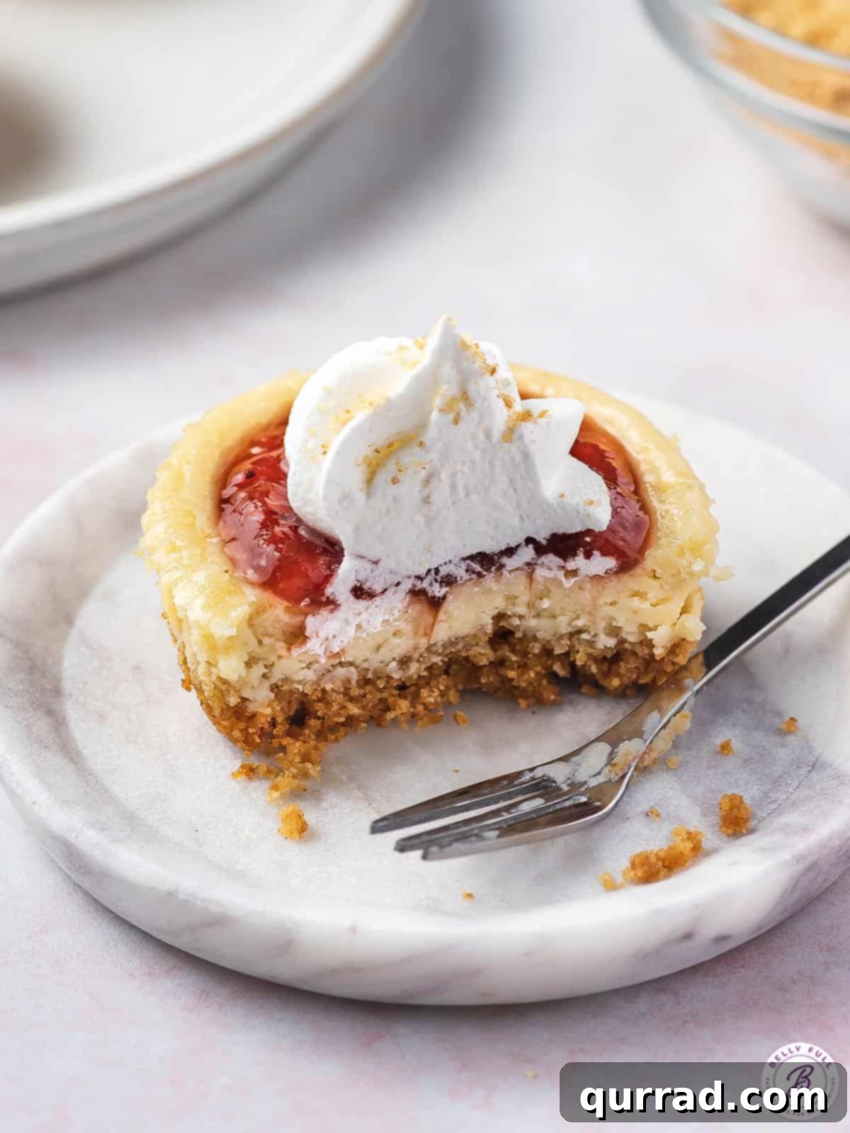 Petite Cheesecakes 5 A small cheesecake sliced in half, revealing its creamy texture and crust, placed delicately on a plate with a fork.