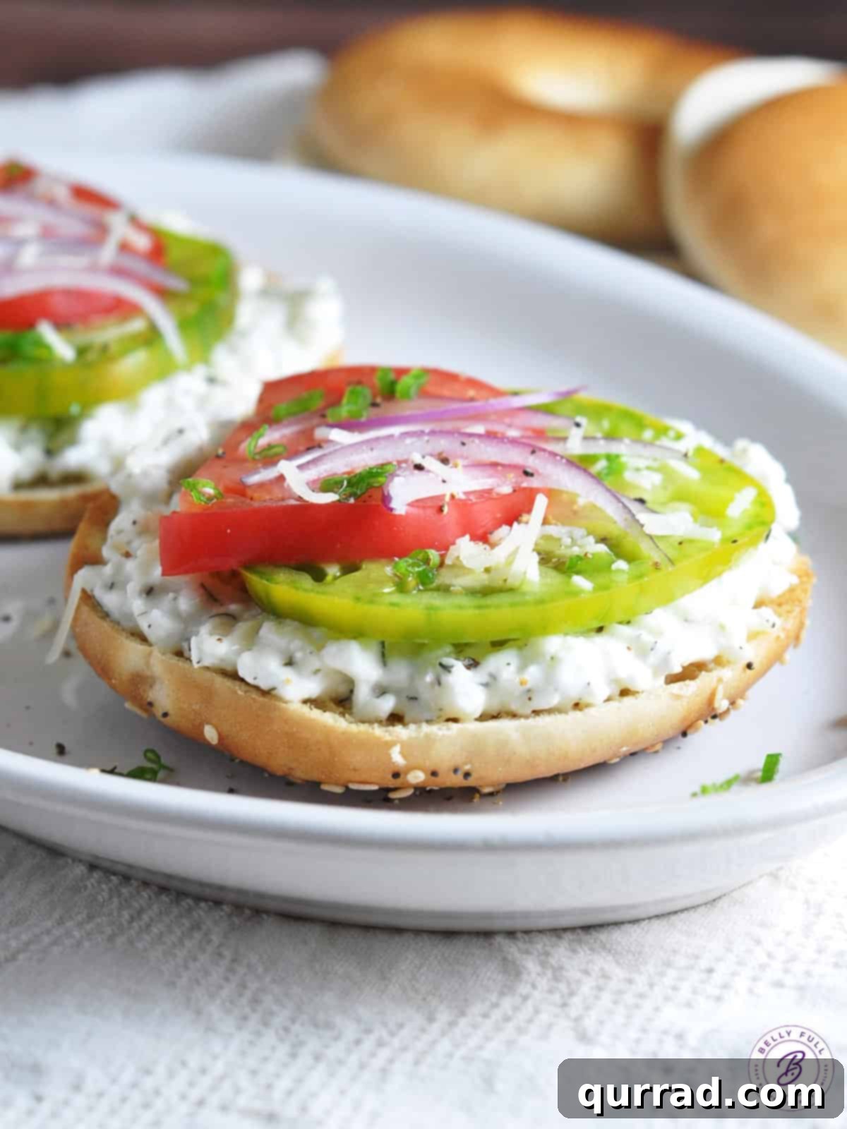 Heirloom Tomato Tartine 2 Freshly toasted bagel topped with herbed cottage cheese, vibrant heirloom tomatoes, and grated Parmesan, ready for a healthy and satisfying breakfast or snack.