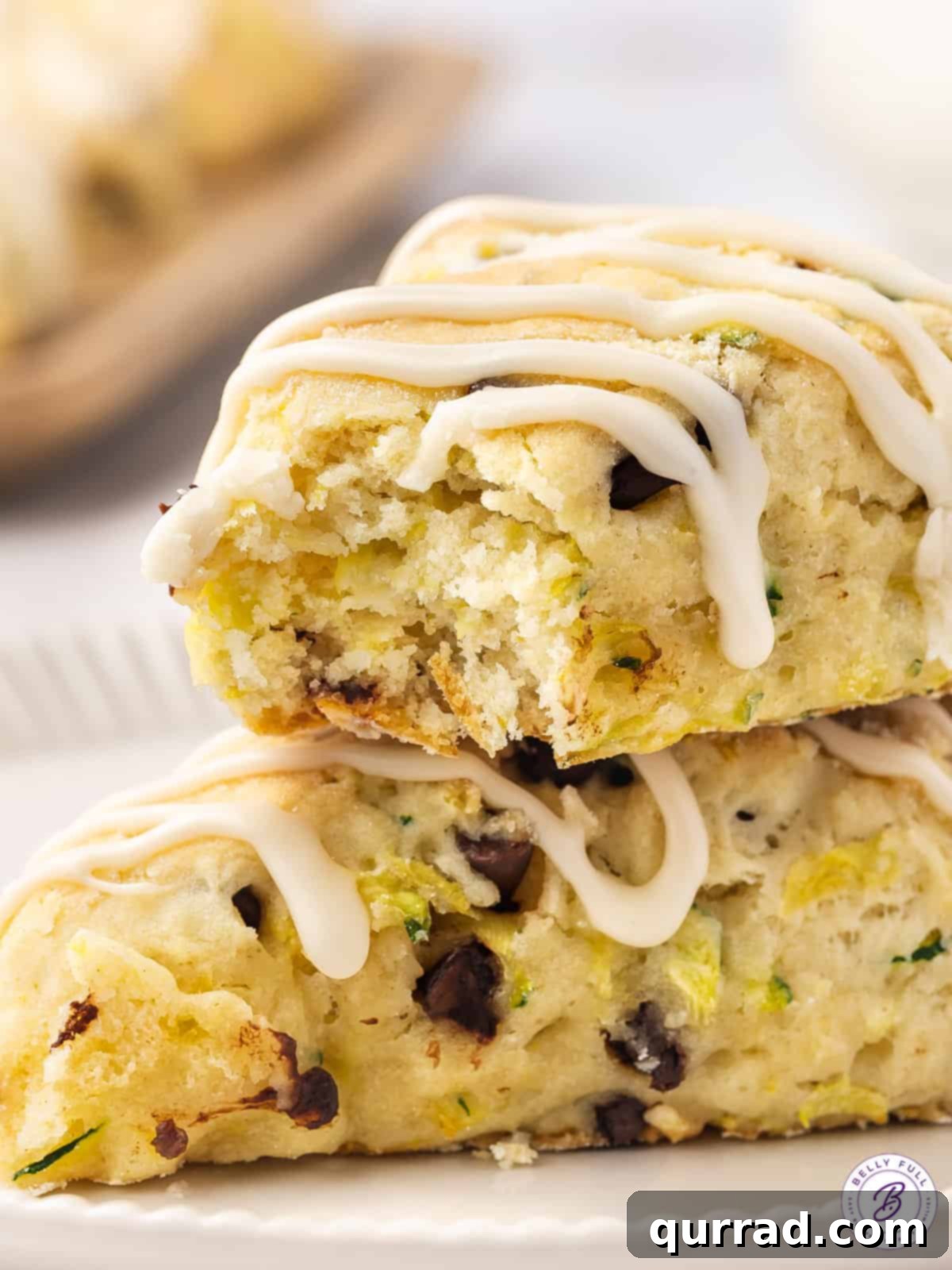 Tender Zucchini Chocolate Chip Scones 5 Two chocolate chip zucchini scones stacked on top of each other, with a bite taken out of the top one, showing the interior texture.
