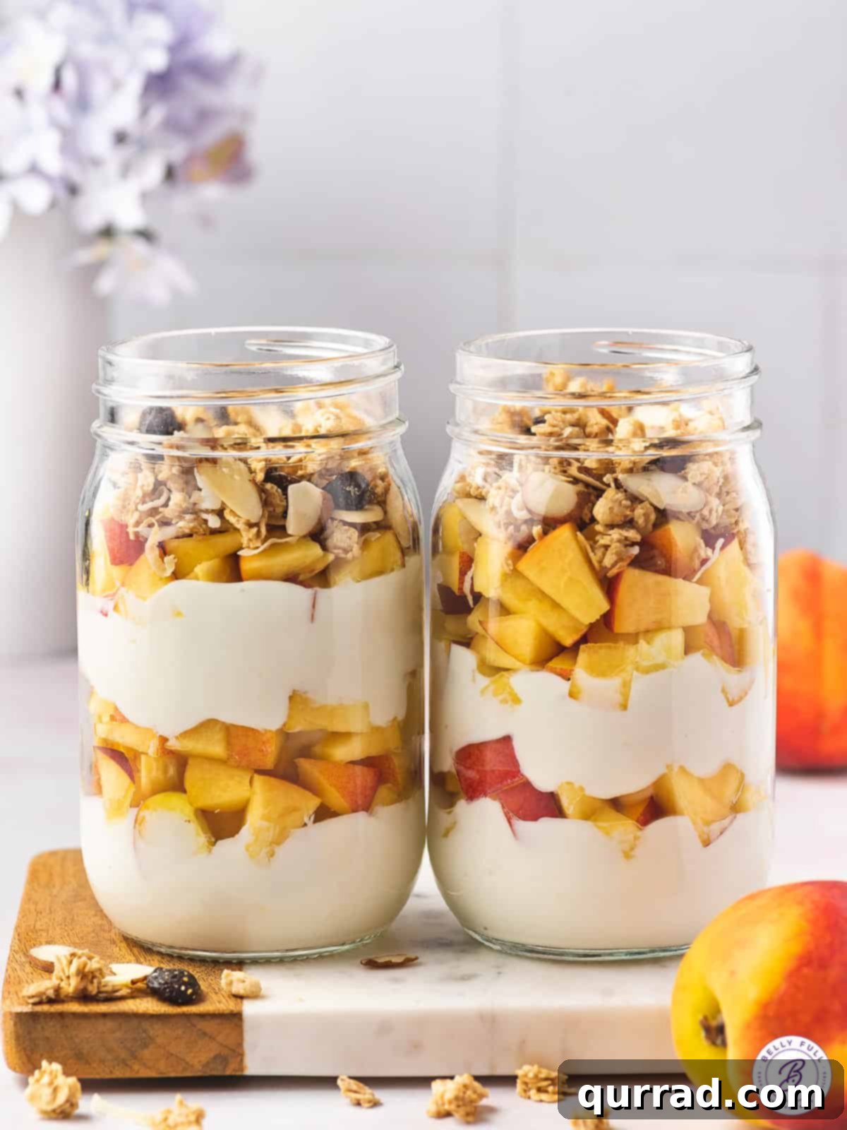 Two clear glass jars filled with perfectly layered peach yogurt parfaits, featuring creamy yogurt, vibrant peach chunks, and golden granola for a satisfying texture.