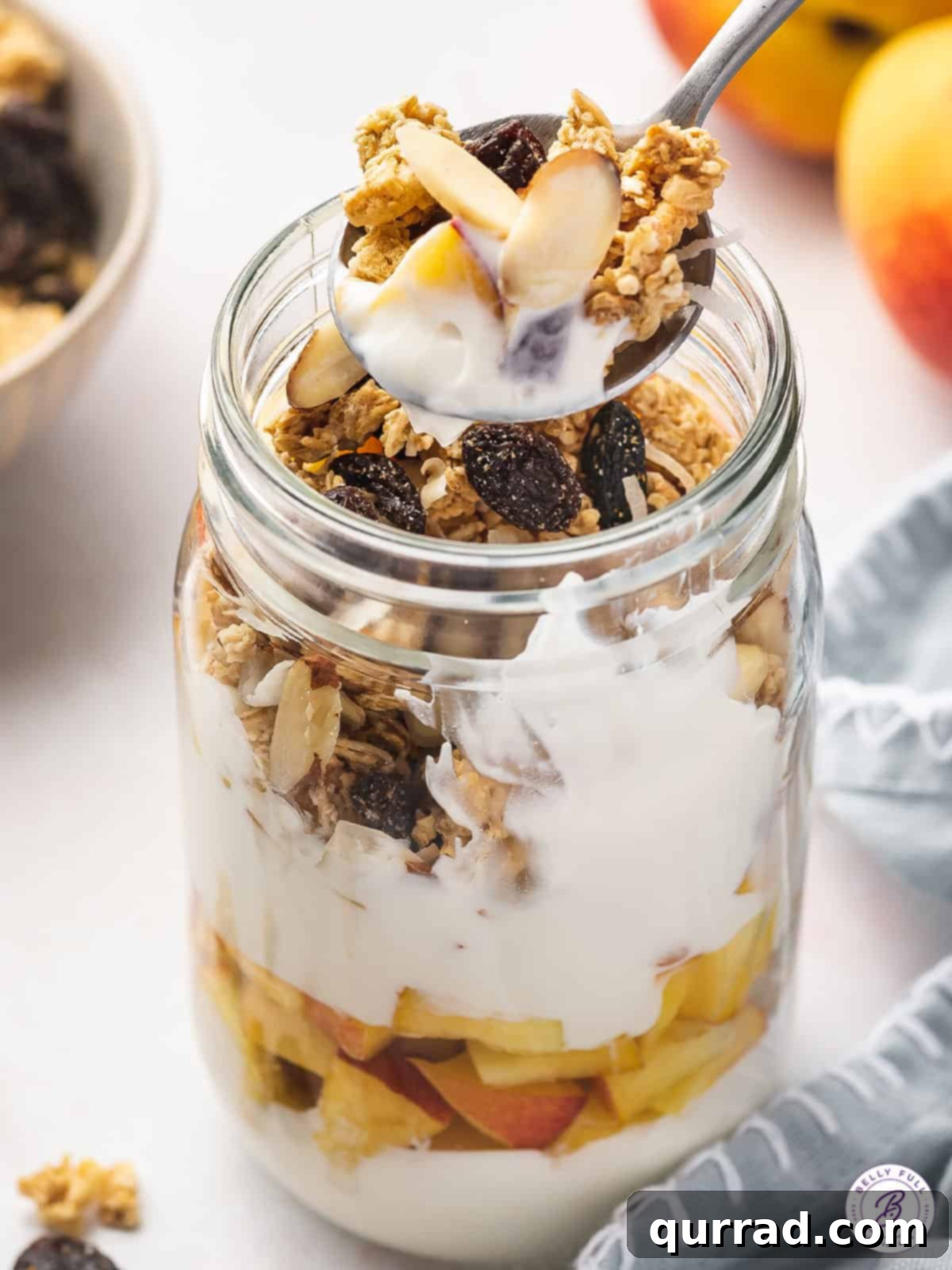 A spoon loaded with layers of creamy yogurt, crunchy granola, and slivered almonds, illustrating the delightful texture combination in a parfait.