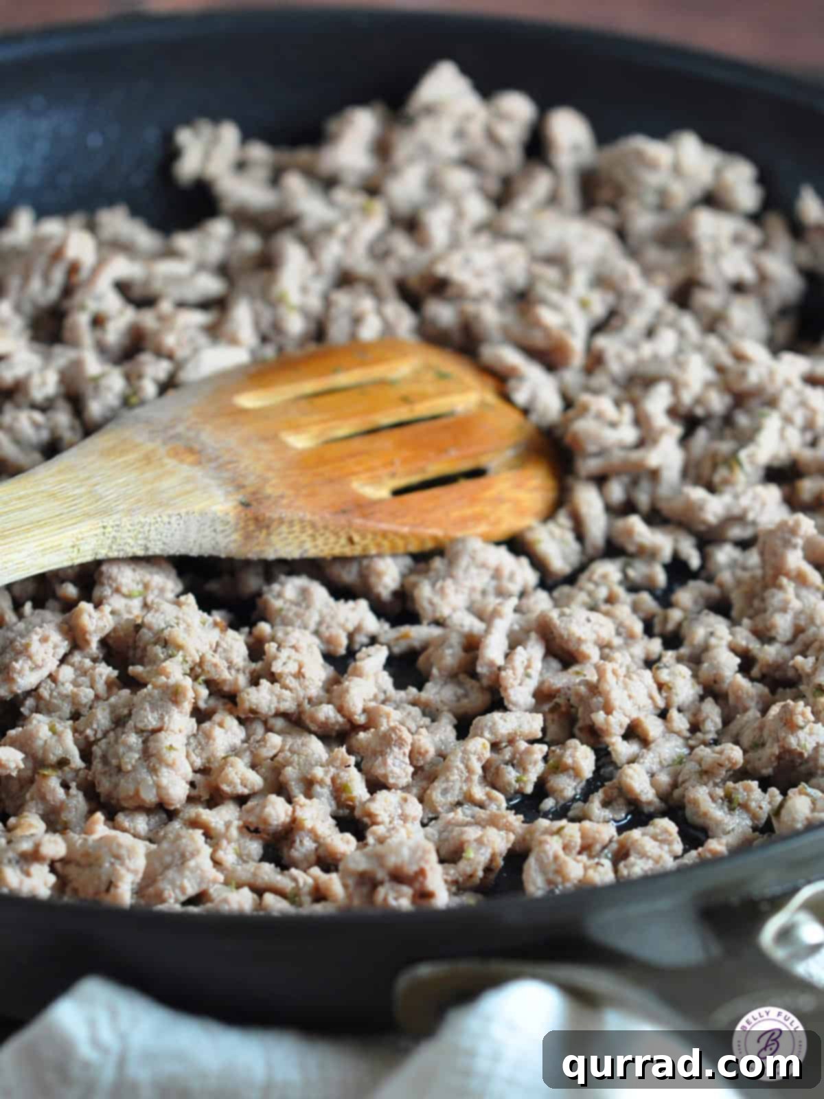 Cooked ground turkey crumbles being stirred in a skillet with seasonings