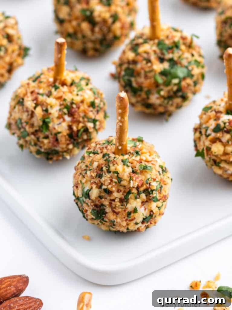Close-up of mini cheese balls coated in crushed nuts with a pretzel stick, showcasing their irresistible texture and perfect size for individual servings.