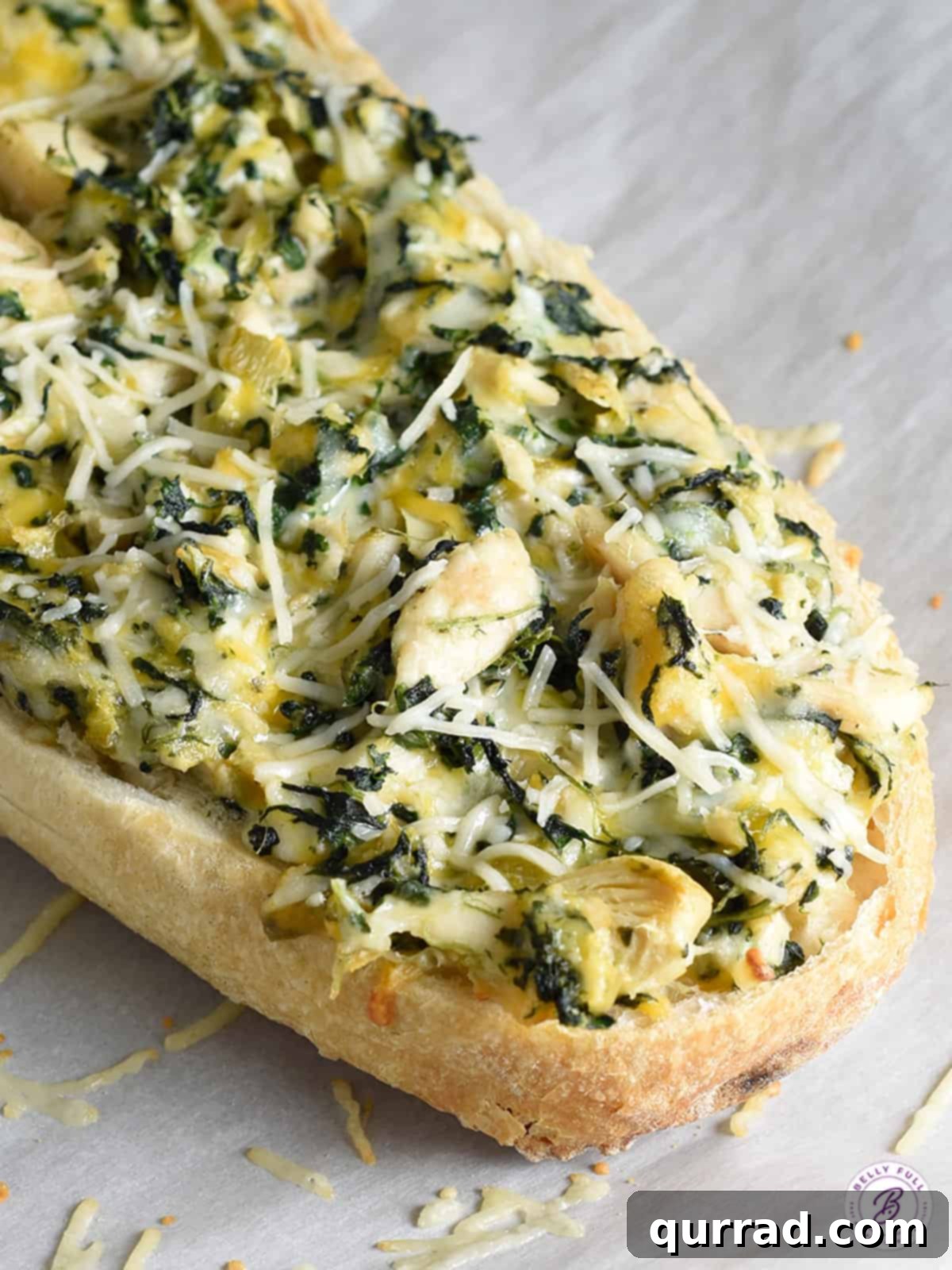 Half a loaf of Spinach Artichoke French Bread Pizza, already cut into individual slices, displaying the melted cheese and a hint of the green filling, on a baking sheet.