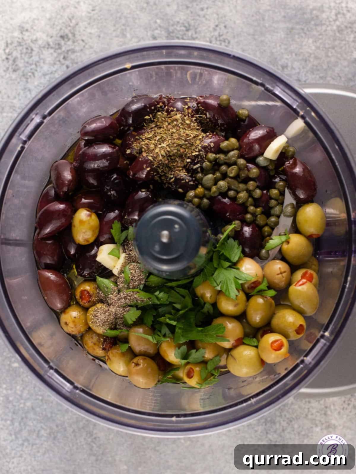 Savory Olive Spread 4 olives, capers, garlic, and fresh herbs in a food processor bowl, ready to be blended