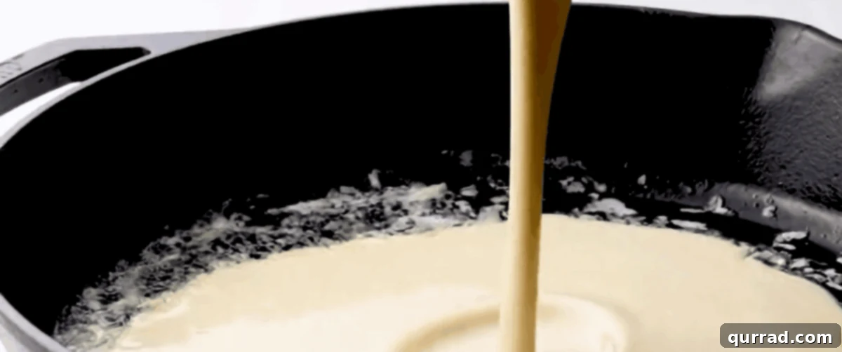 Pouring smooth Dutch Baby pancake batter into a hot, buttered cast iron skillet.