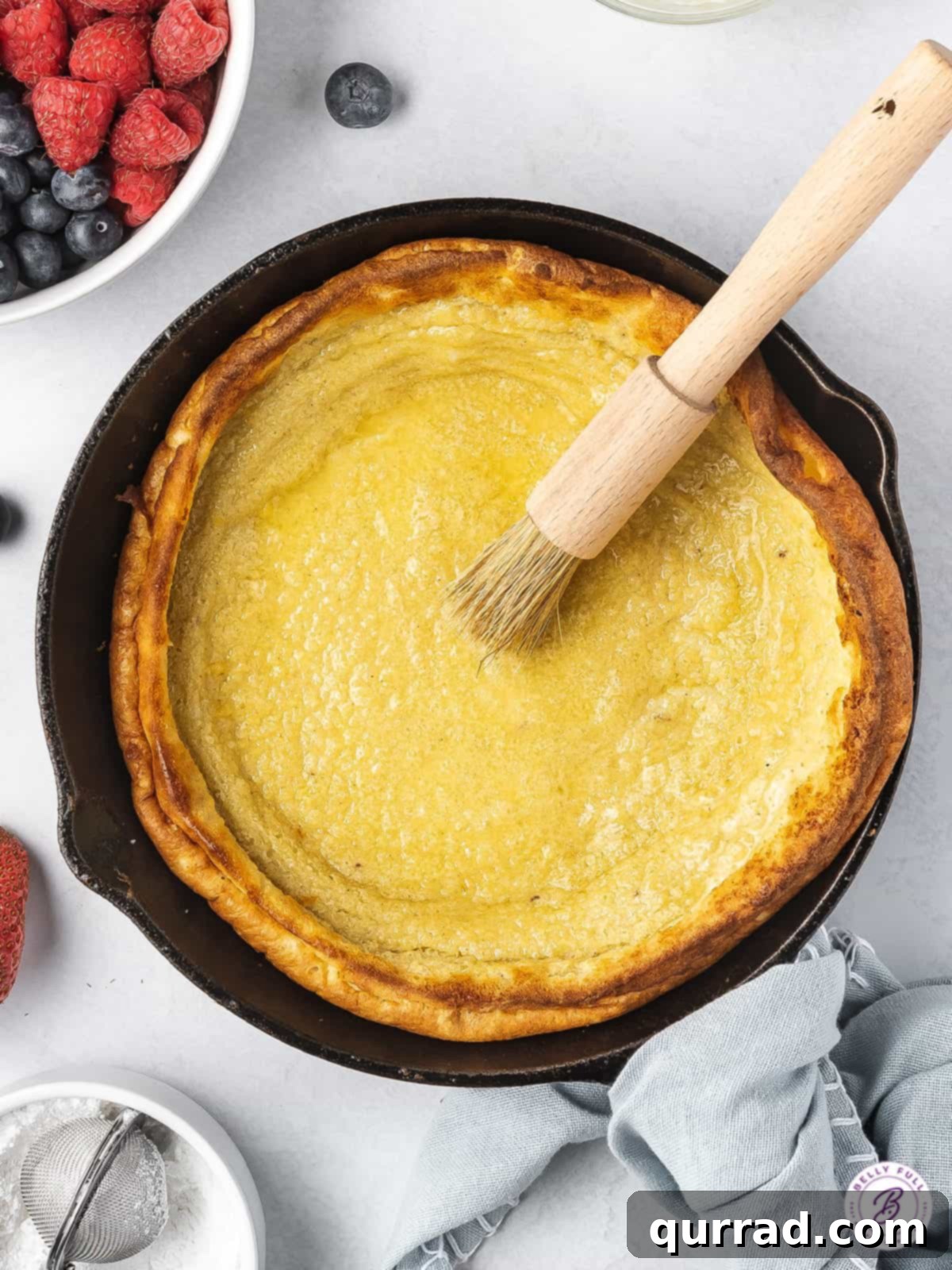 Freshly baked Dutch Baby German pancake in a skillet being brushed with melted butter.