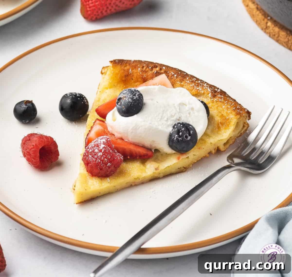 A slice of Dutch Baby pancake on a plate, topped with mixed berries and a dollop of whipped cream.