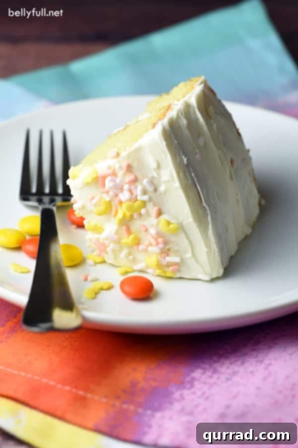 Surprise Inside Piñata Cake 4 A close-up shot of a single slice of Piñata Cake on a white plate, showcasing the colorful M&Ms and other candies tumbling out of its carved-out center.